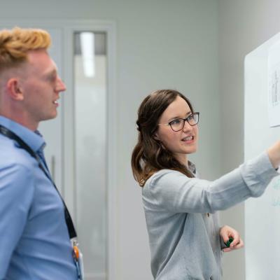 a man and woman talk something out while writing on a white board